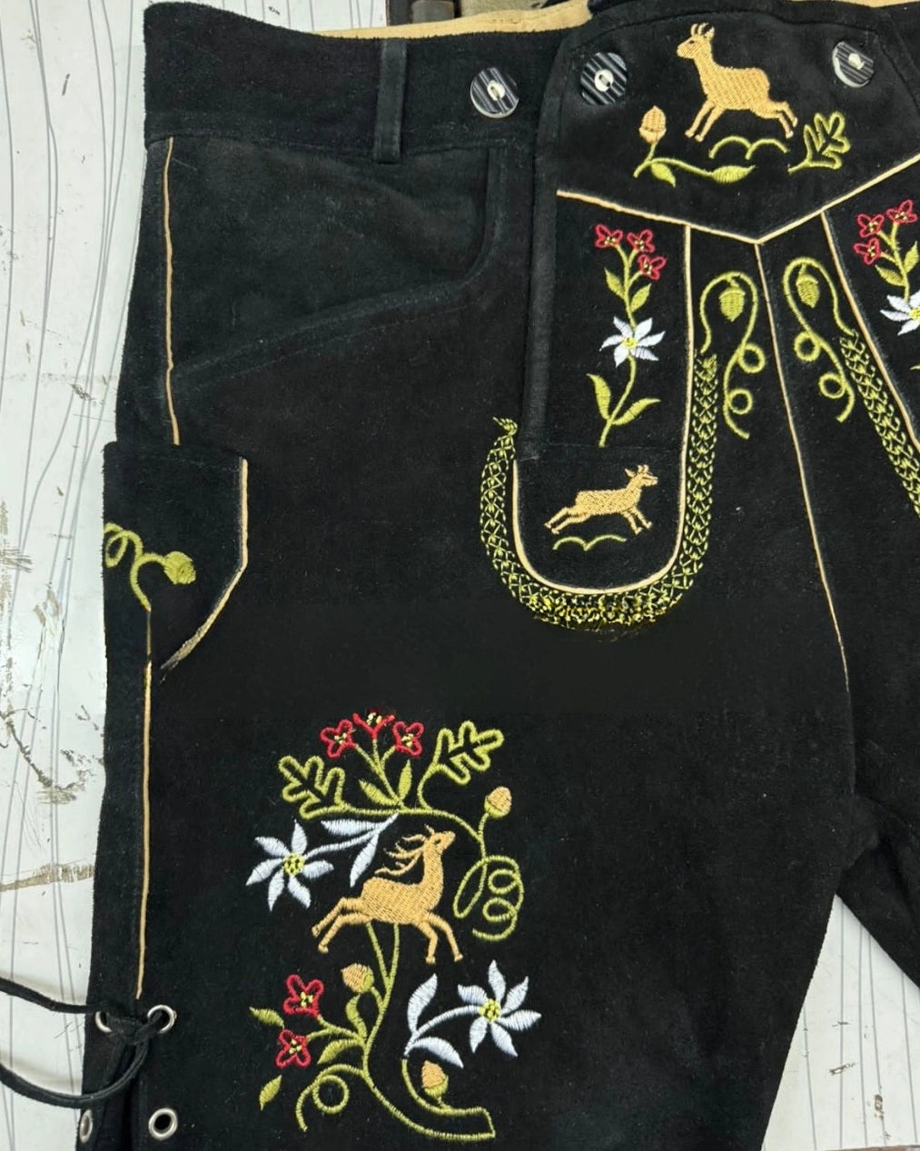 Black pants with intricate embroidery of deer and flowers on a white background