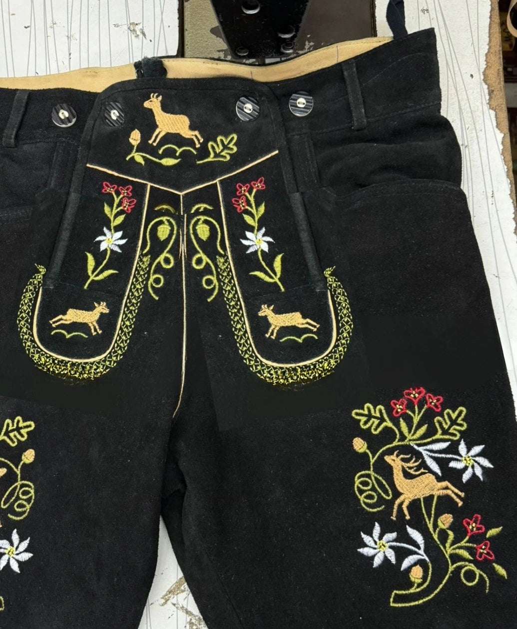 Black pants with intricate embroidery featuring animals and flowers on a wooden surface.