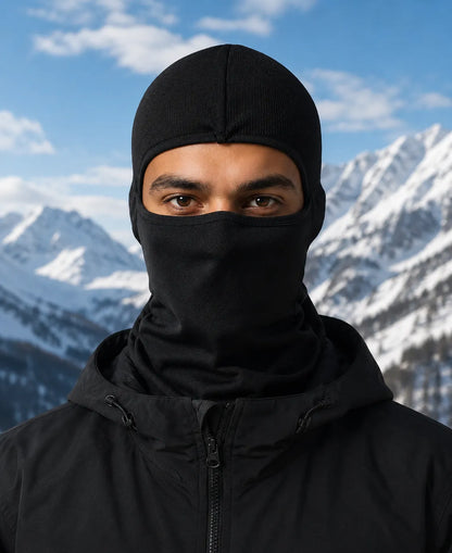 Person wearing a black balaclava and jacket against a mountainous background