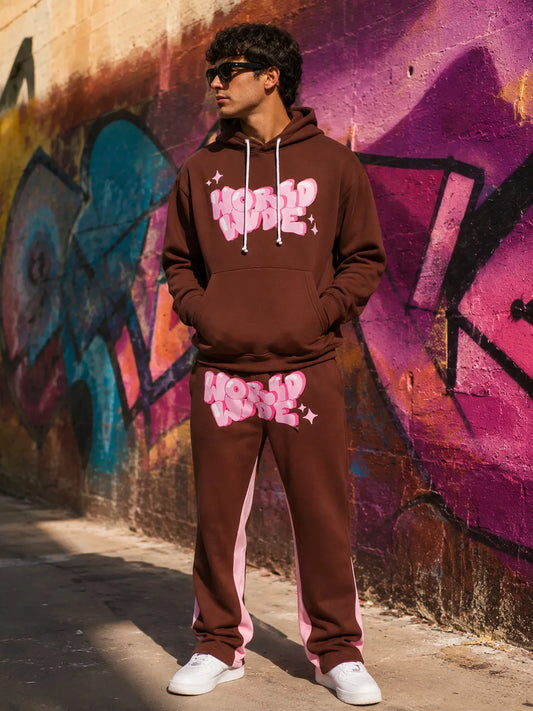 Person wearing a brown tracksuit with pink text in front of a graffiti wall.