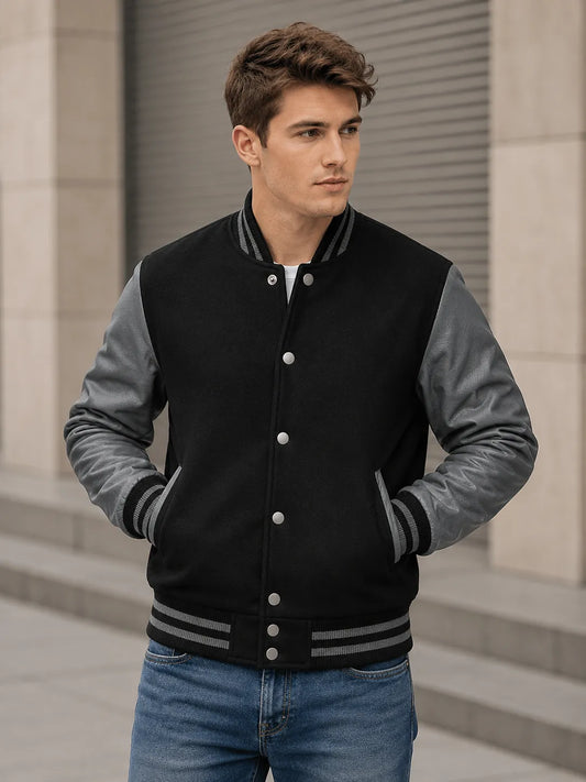 Man wearing a black and gray varsity jacket standing outdoors.