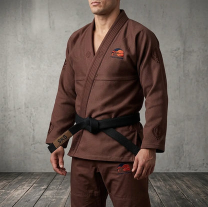 Person wearing a brown martial arts uniform with logos against a gray concrete wall.