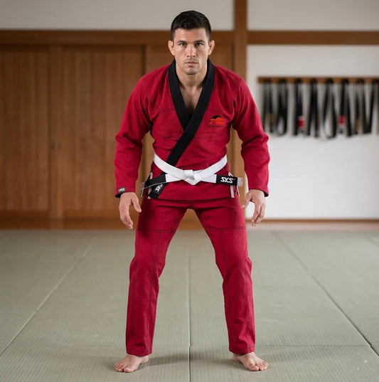Man in red martial arts uniform with white belt standing in a dojo.