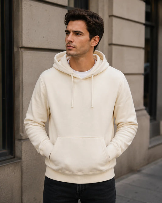 Man wearing a white hoodie standing against a gray building.