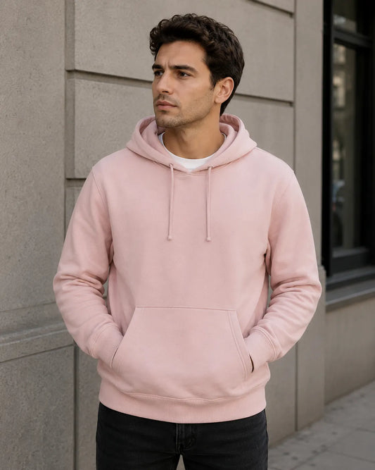 Man wearing a pink hoodie standing against a neutral wall.
